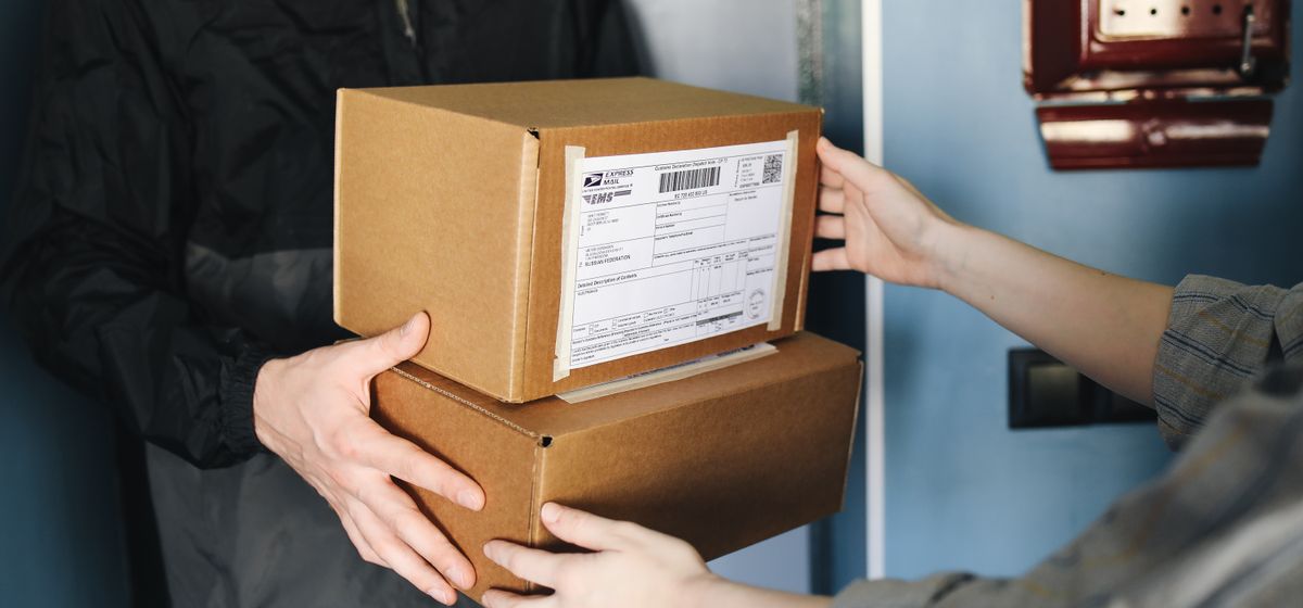 Mãos trocando caixas de papelão, representando serviço de entrega